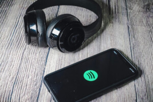 Sitting on a wooden surface, a Spotify app is open on a cellphone beside a pair of headphones.